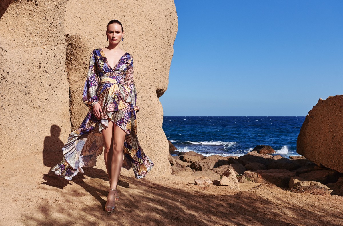 mpresionante vestido largo cruzado con falda con volantes asimetrica en satén estampado geométrico en tonos lilas, morados, verdes y amarillos para invitadas a boda de verano